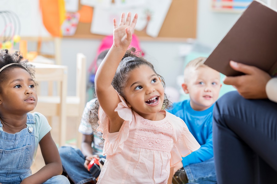 A child raising hands in class with a smile